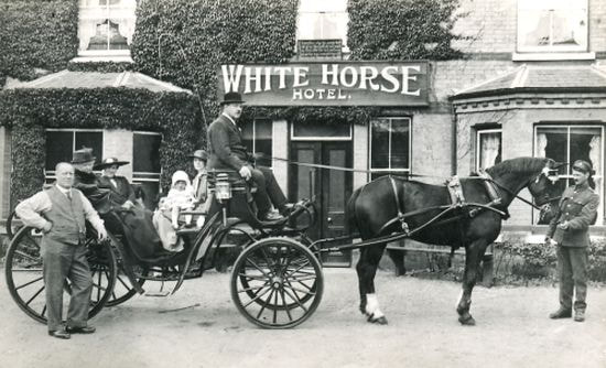 The White Horse Hotel in the 1910s. The baby in the carriage is George Spalding whose father and then his
mother were the landlords.  By 1959 it was George's turn to continue the family tradition.
He is with his mother Viola, his father Harry is standing on the left and his two stepsisters
are sitting in the carriage.  In the garden at the back of the hotel he had some chalets built
and transformed a Nissen hut into a Pavilion which he hired out for many a charitable function.
He brought in coachloads of tourists and established cabaret evenings for their entertainment.
In the 1970s the pavilion burnt down and George left The White Horse in 1976 to move into
and manage the Uplands Hotel, across the road.